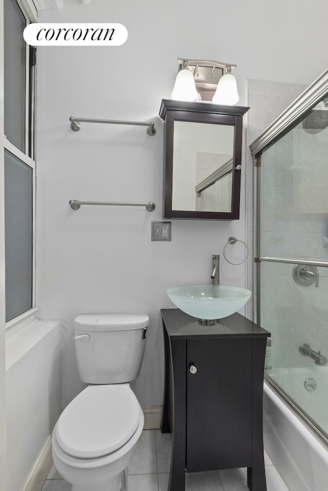 bathroom with tile patterned floors, toilet, shower / bath combination with glass door, baseboards, and vanity