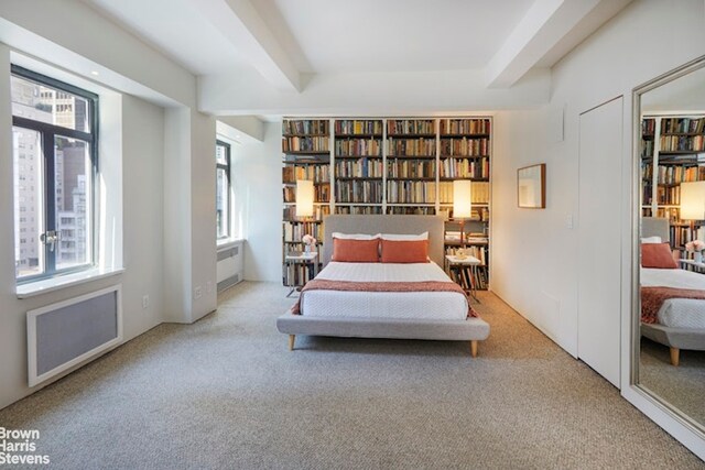 bedroom featuring light colored carpet, radiator heating unit, and beam ceiling