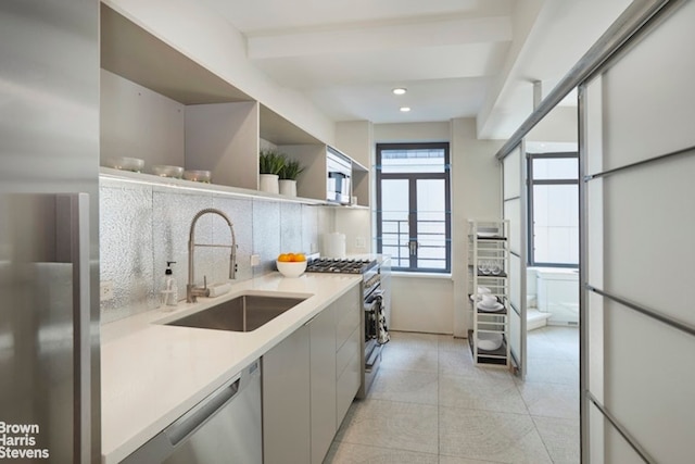 kitchen with open shelves, light countertops, backsplash, appliances with stainless steel finishes, and a sink