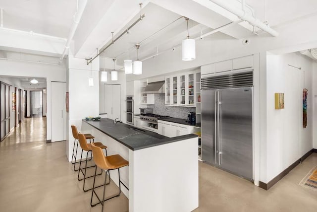 kitchen featuring pendant lighting, wall chimney range hood, stainless steel appliances, and white cabinets