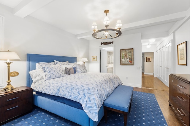 bedroom featuring baseboards, ensuite bath, wood finished floors, an inviting chandelier, and beam ceiling