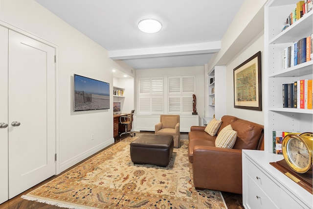 living area featuring built in shelves, beam ceiling, and baseboards