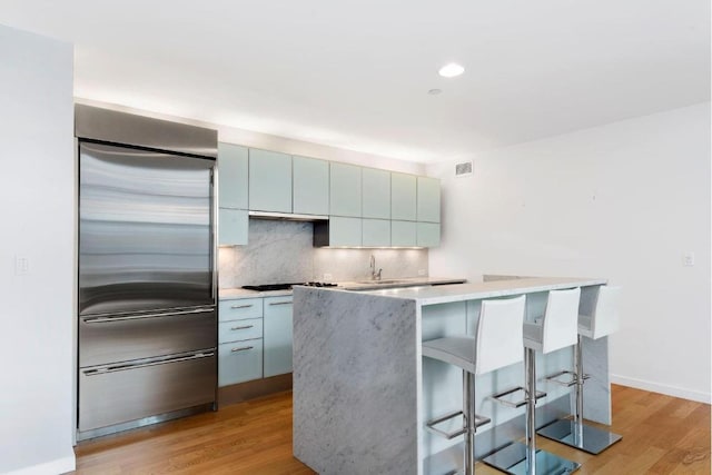 kitchen featuring a center island, decorative backsplash, built in fridge, and light wood-type flooring