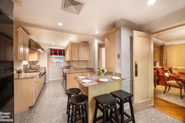 kitchen featuring visible vents, a breakfast bar, recessed lighting, light brown cabinetry, and wall chimney range hood