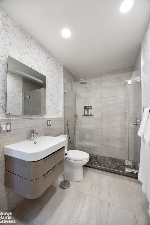 bathroom with vanity, toilet, tile walls, and a shower with shower door