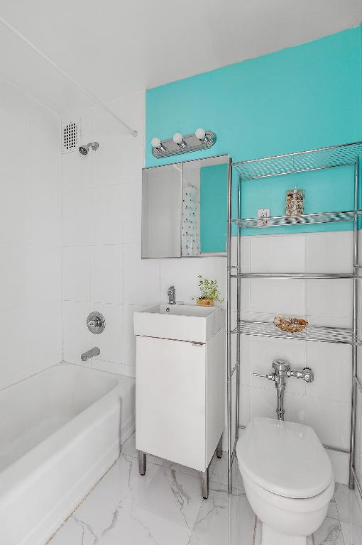 full bathroom with tiled shower / bath, vanity, toilet, and tile walls