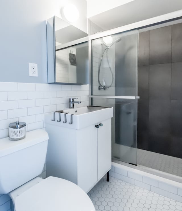 bathroom with walk in shower, toilet, tile walls, vanity, and tile patterned flooring