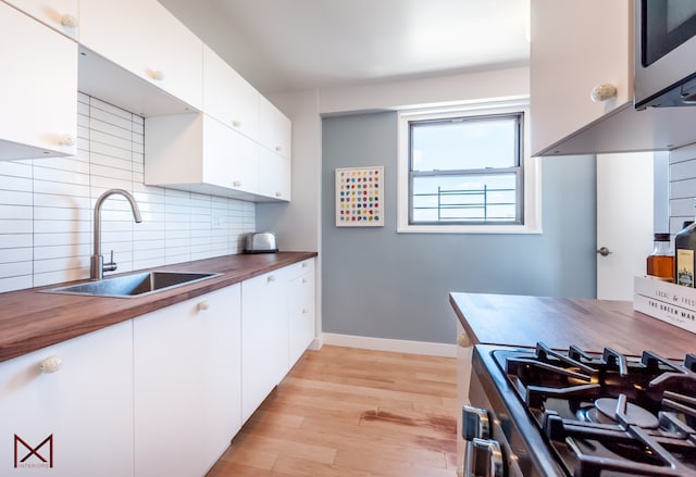 kitchen featuring light wood finished floors, a sink, backsplash, wood counters, and appliances with stainless steel finishes