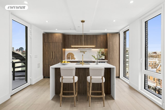 kitchen with light wood-type flooring, a center island with sink, hanging light fixtures, a breakfast bar, and sink