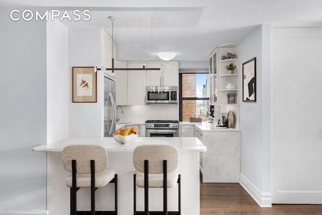 kitchen with appliances with stainless steel finishes, white cabinetry, sink, decorative backsplash, and kitchen peninsula