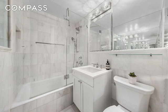 full bathroom featuring toilet, vanity, bath / shower combo with glass door, and tile walls