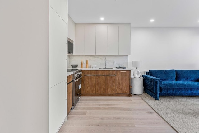 kitchen featuring sink, white cabinetry, tasteful backsplash, stainless steel stove, and light hardwood / wood-style floors