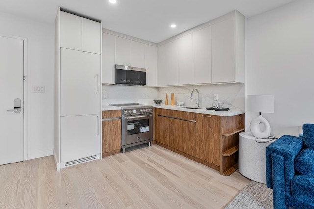 kitchen with sink, white cabinetry, backsplash, high end stainless steel range, and light wood-type flooring