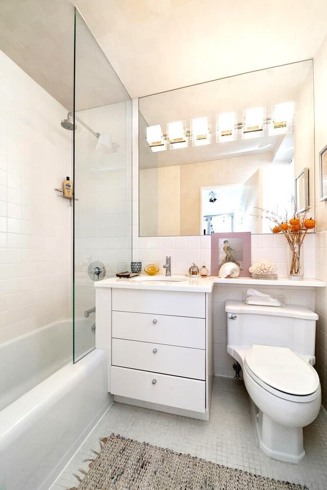 full bathroom featuring tile walls, tile patterned flooring, vanity, tiled shower / bath, and toilet