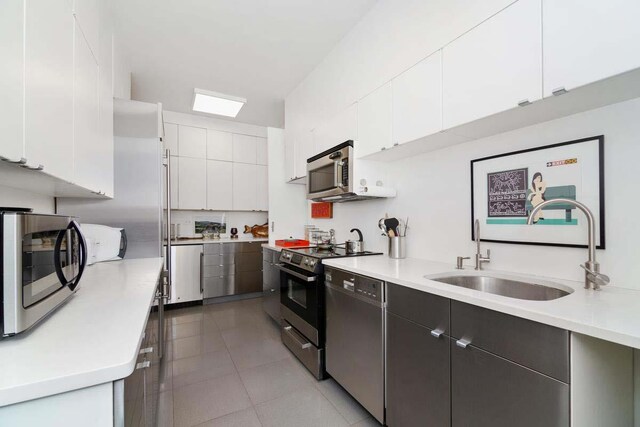 kitchen with sink, light tile patterned floors, white cabinets, and appliances with stainless steel finishes