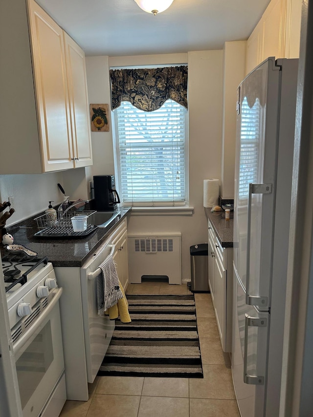 kitchen with white range with gas cooktop, radiator heating unit, white cabinetry, freestanding refrigerator, and light tile patterned floors