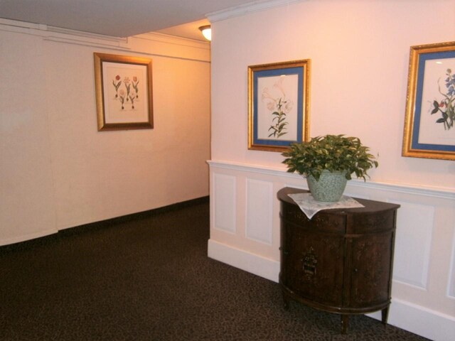 hallway with ornamental molding, dark carpet, and a decorative wall