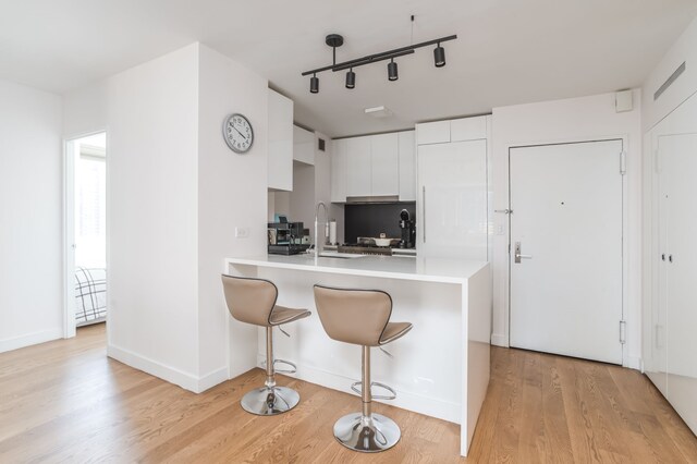 kitchen featuring white cabinetry, sink, a breakfast bar area, kitchen peninsula, and light wood-type flooring