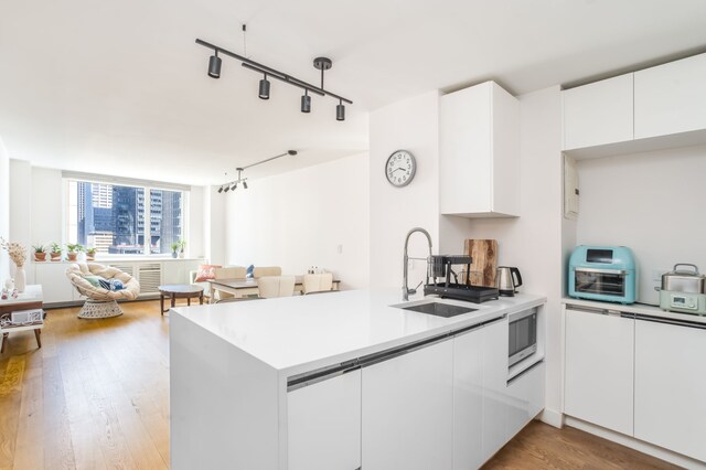 kitchen with sink, white cabinetry, hardwood / wood-style floors, stainless steel microwave, and kitchen peninsula