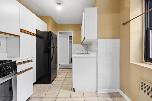 kitchen with light tile patterned flooring, sink, black fridge, white cabinetry, and stainless steel range with gas cooktop