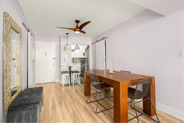 dining space with ceiling fan, a barn door, and light hardwood / wood-style floors