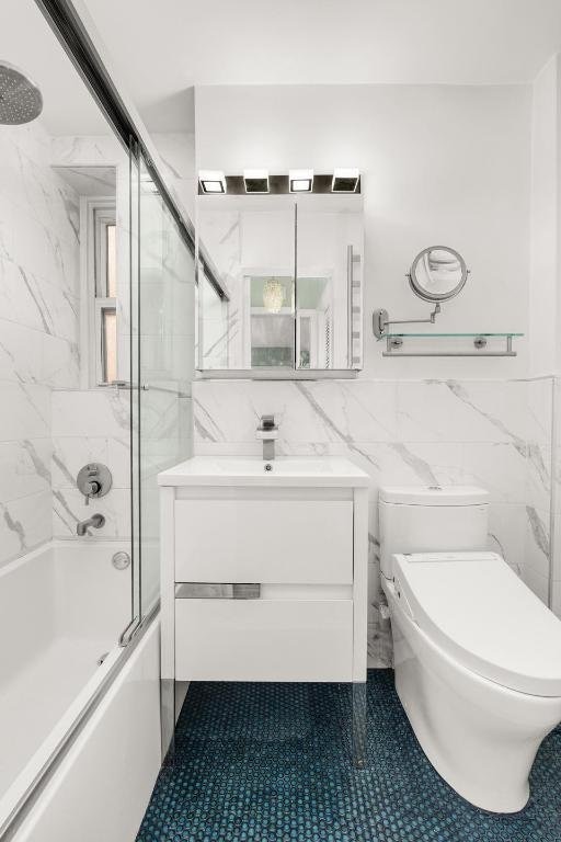 full bathroom with vanity, toilet, combined bath / shower with glass door, and tile walls