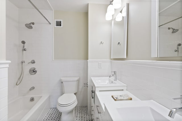 bathroom featuring visible vents, a wainscoted wall, toilet, a sink, and tile walls