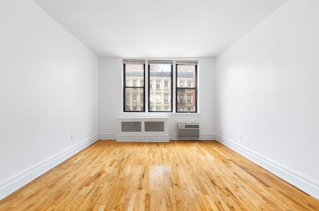 empty room featuring a wall unit AC, baseboards, and wood finished floors