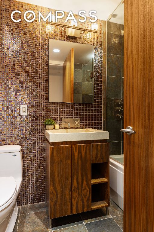 full bathroom with tiled shower / bath, tile walls, vanity, and toilet