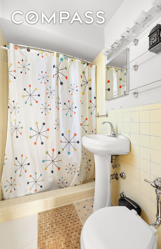 bathroom featuring toilet, curtained shower, a sink, and tile walls