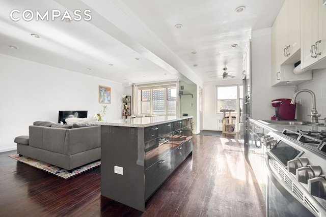 kitchen with a sink, white cabinets, stainless steel gas range, a center island, and dark wood finished floors