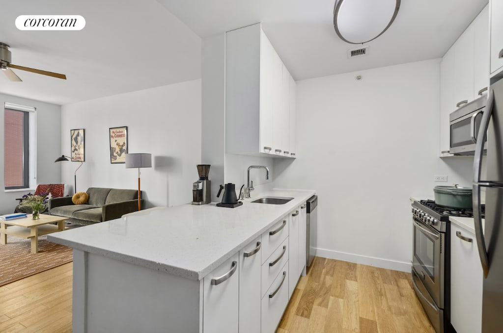 kitchen featuring appliances with stainless steel finishes, sink, white cabinets, and light hardwood / wood-style flooring