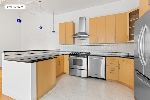 kitchen featuring dark countertops, a peninsula, marble finish floor, stainless steel appliances, and wall chimney range hood