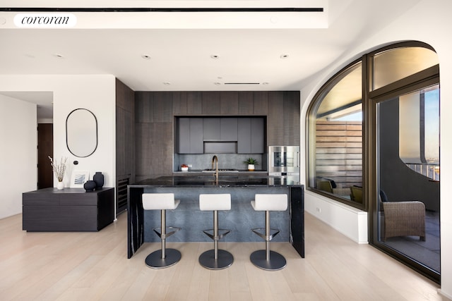 kitchen with a breakfast bar area, modern cabinets, light wood-type flooring, visible vents, and decorative backsplash