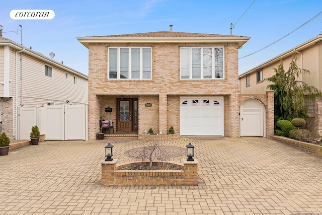 view of front of house with an attached garage, fence, brick siding, a gate, and decorative driveway