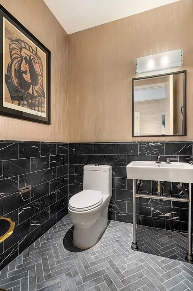 bathroom featuring toilet, tile walls, a sink, and a wainscoted wall