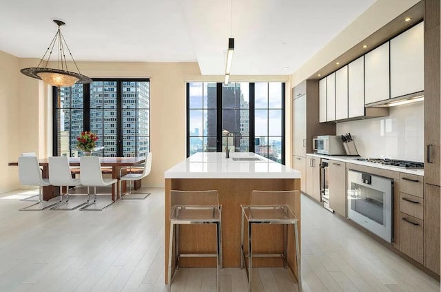 kitchen with white cabinetry, decorative light fixtures, wall oven, stainless steel gas cooktop, and a kitchen island with sink