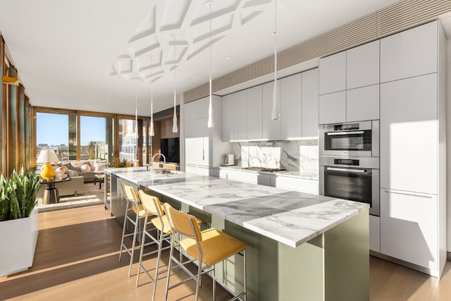 kitchen with a breakfast bar area, appliances with stainless steel finishes, an island with sink, light hardwood / wood-style floors, and white cabinets