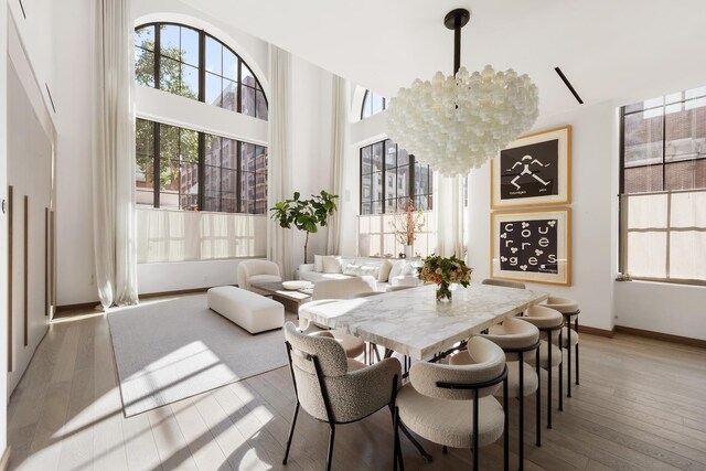 dining room featuring a notable chandelier, a towering ceiling, and light hardwood / wood-style floors