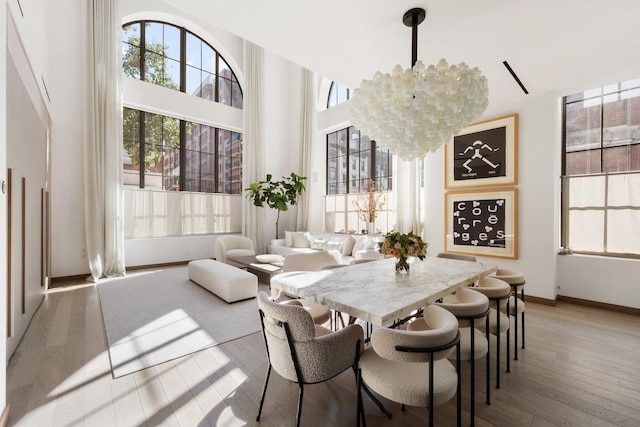 dining area featuring baseboards, a notable chandelier, a towering ceiling, and hardwood / wood-style floors