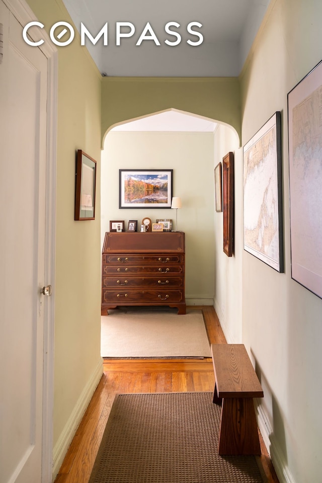 hallway with wood finished floors, baseboards, and arched walkways