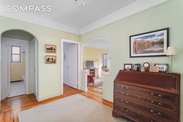 hall with arched walkways, baseboards, and light wood-style floors