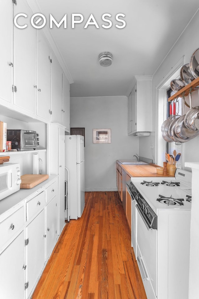 kitchen with white appliances, white cabinetry, light countertops, and a sink