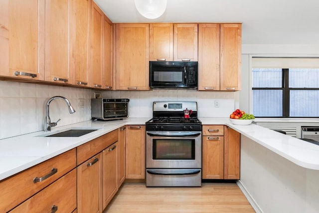 kitchen featuring tasteful backsplash, sink, stainless steel gas range oven, light stone countertops, and light wood-type flooring