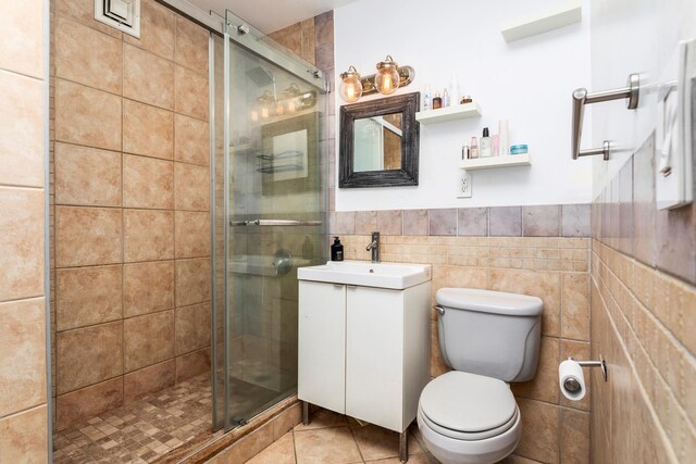 bathroom featuring tile patterned floors, toilet, a shower with shower door, and tile walls