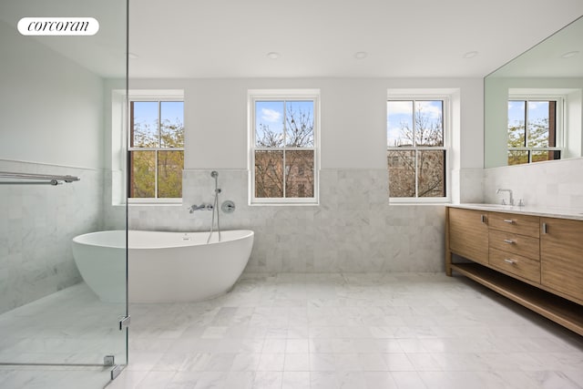 bathroom with vanity, a wainscoted wall, visible vents, a soaking tub, and tile walls