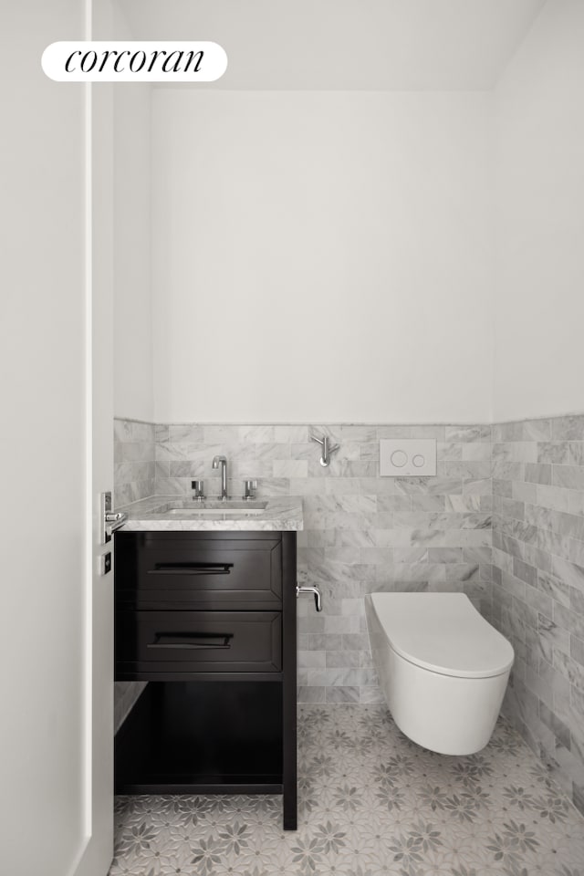 half bathroom with toilet, tile walls, wainscoting, and vanity