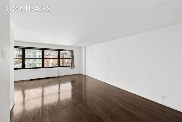 unfurnished room featuring radiator, wood finished floors, and baseboards