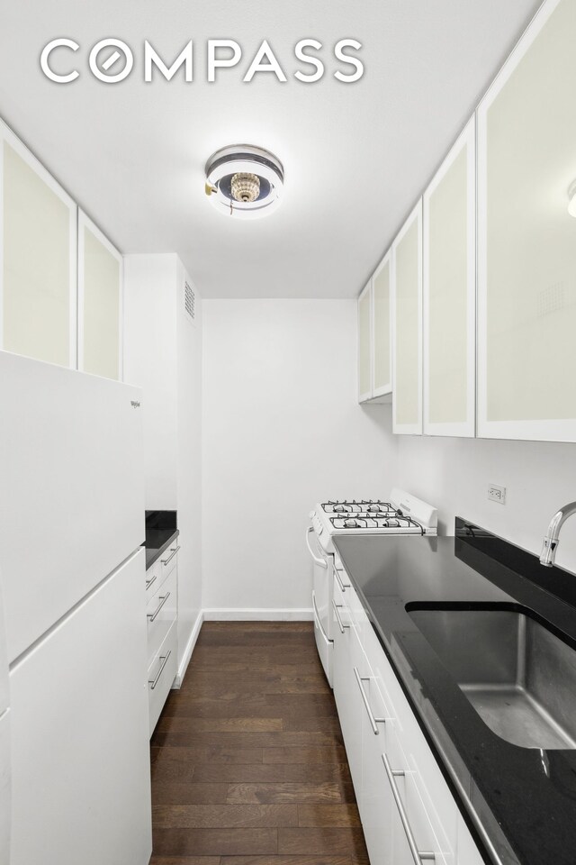 kitchen with dark countertops, white appliances, white cabinetry, and dark wood-style flooring