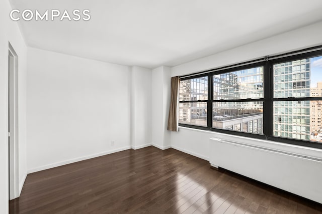 unfurnished room with a wealth of natural light, dark wood-type flooring, a city view, and radiator heating unit